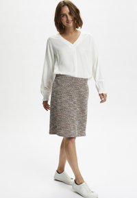 White, long-sleeve, v-neck blouse paired with a textured, mid-length skirt featuring blue and orange stripes. White sneakers complete the look.