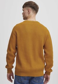 Yellow ribbed sweater with a crew neck, featuring textured fabric and long sleeves. Worn with blue jeans, viewed from the back.