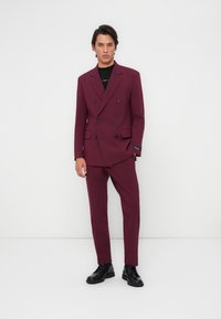 Completo bordeaux doppiopetto con rever a punte, pantaloni abbinati e scarpe nere stringate. Presenta una vestibilità elegante e su misura.