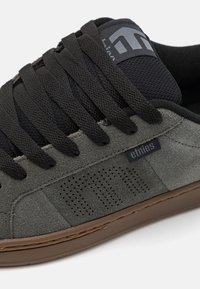Sneaker in suede nero e grigio con suola in gomma, dotata di lacci spessi, linguetta in tessuto e pannelli laterali perforati per la ventilazione.