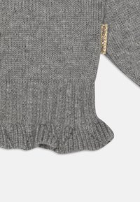 Maglione grigio lavorato a maglia con orlo a coste e accento svasato. Presenta un piccolo etichetta dorata sulla manica. Finitura testurizzata, filato morbido.