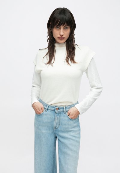 Λευκή υφασμάτινη μπλούζα με κοντό μανίκι, φορεμένη πάνω από πουκάμισο με μακριά μανίκια. Συνδυασμένη με ανοιχτόχρωμο γαλάζιο τζιν ψηλόμεσο με κούμπωμα κουμπιού.