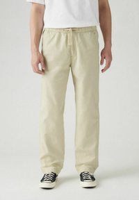 Lichtbeige, broek met trekkoord uit zachte stof. Ontspannen pasvorm met zijzakken. Gecombineerd met zwart-witte sneakers.