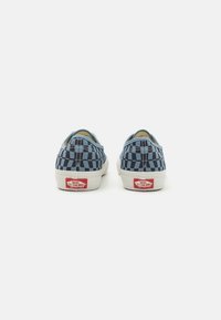 Blauwe en zwarte geblokte instappers met een solide teenkap en witte rubberen zool. Heeft een rode Vans-logo op de hiel.