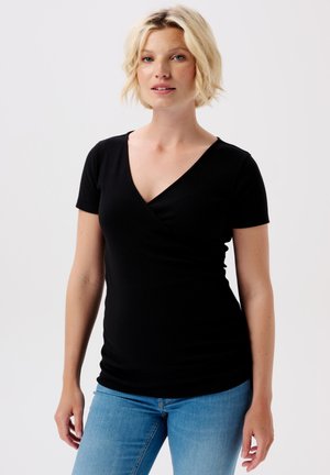 Schwarzes kurzärmliges Wickeltop mit V-Ausschnitt, aus geripptem Stoff. Das Modell kombinierte es mit hellblauen Jeans.