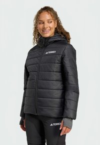 Juoda pūkinė striukė su kapišonu, siuvinėtu raštu, su užtrauktuku ir Terrex logotipu kairėje krūtinės pusėje. Tinka lauko veiklai.