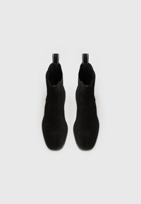 Bottines en daim noir avec une texture lisse, bout carré et tirettes contrastantes. Design léger avec un style minimaliste.