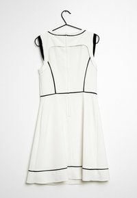 Bílá bezramínková šaty s černými lemy, obepnutou korzetovou částí, rozšířenou sukní a zipovým zapínáním na zadní straně. Visí na černém háčku.