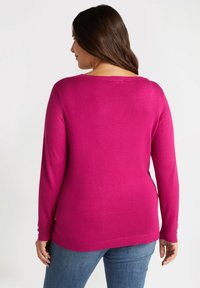 Fuksjowy sweter z długimi rękawami, ściągaczami przy mankietach i u dołu. Miękka faktura i luźny krój. Tył ukazuje okrągły dekolt i lekko przedłużony tył.