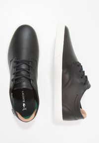 Black leather lace-up shoes with white rubber soles. Features a green and beige insole, smooth texture, and minimalistic design.