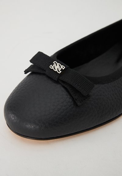 Schwarze Leder-Ballettschuhe mit strukturiertem Finish, einem kleinen schwarzen Schleifenbogen und einem silbernen Dekorationsdetail auf der Schleife.
