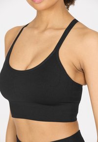 Schwarzes Crop-Top aus elastischem Material. Es hat dünne Träger, einen runden Ausschnitt und eine nahtlose Oberfläche mit einem figurschmeichelnden Schnitt.