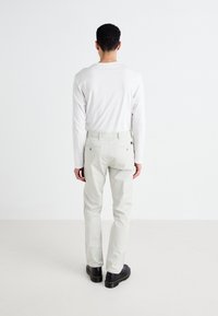 Lys grå bukser med to baklommer, brukt med en hvit langermet skjorte. Buksene har en rett ben-design og minimal detaljering.