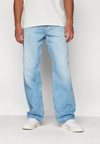 Jeans de denim azul claro con un corte relajado, que presentan una pierna recta, un desvanecimiento sutil y un diseño estándar de cinco bolsillos. Llevados con zapatillas blancas.