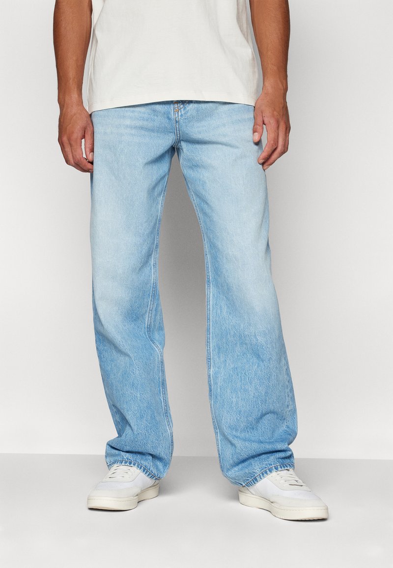Jeans de denim azul claro con un corte relajado, que presentan una pierna recta, un desvanecimiento sutil y un diseño estándar de cinco bolsillos. Llevados con zapatillas blancas.