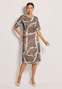 Knielanges Kleid aus weichem Stoff mit einem geometrischen Muster in Braun, Creme und Schwarz. Mit kurzen Ärmeln und rundem Halsausschnitt.