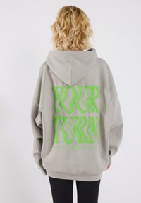 Overdimensjonert grå hettegenser med grønn tekst "DIN TUR" på baksiden, mykt stoff, frontlomme med kenguru-design og snorhette.