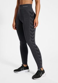 Czarne legginsy o wysokim stanie z fakturowanym wzorem i chevronowym wzorem w jaśniejszym odcieniu po bokach. W połączeniu z czarnymi butami sportowymi.