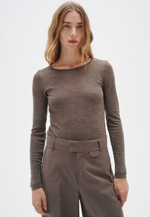 Haut marron à manches longues avec un col rond, fabriqué à partir d'un tissu texturé, associé à un pantalon grisé taille haute et ajusté avec une ceinture.