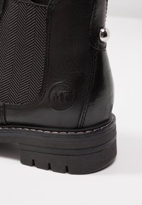 Zwarte leren enkellaars met textuur, stof in ruitpatroon, een ronde neus en een chunky, geribbelde rubberen zool. Bevat metalen hardware.