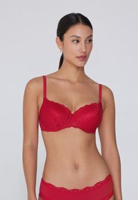 Červená krajková podprsenka s hladkým, vycpaným designem, nastavitelnými ramínky a vlnitými okraji pro detailní texturu a strukturu.