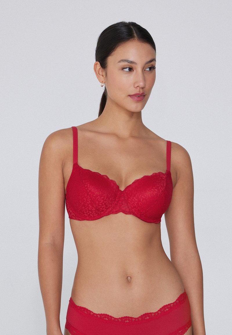 Červená krajková podprsenka s hladkým, vycpaným designem, nastavitelnými ramínky a vlnitými okraji pro detailní texturu a strukturu.
