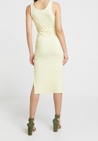 Ribbad, tankklänning i ljusgul med en figursydd silhuett och sidoklyfta. Bärs med gröna, rejäla klacksandaler.