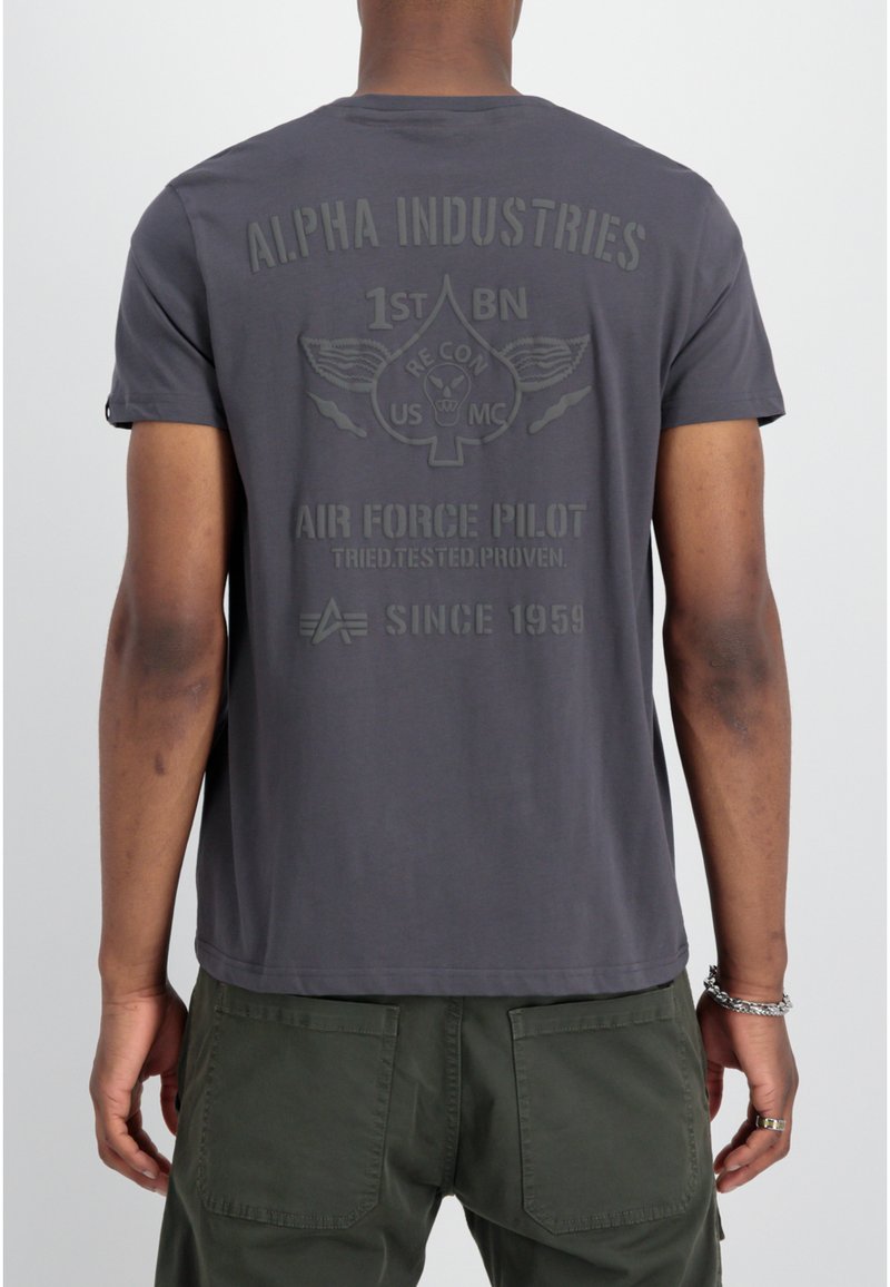 Camiseta de algodón gris con un gráfico en la parte posterior que dice "ALPHA INDUSTRIES AIR FORCE PILOT" junto con un diseño de espada alada. Mangas cortas, cuello redondo.
