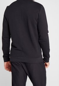 Sudadera negra de tela suave, con cuello redondo, mangas largas, puños y dobladillo acanalados, que presenta un detalle de costura en la parte posterior y un corte relajado.