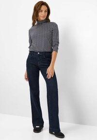 Top a collozzo a righe marinare abbinato a jeans a zampa d'elefante blu scuro. Il top presenta un design geometrico, mentre i jeans hanno una vestibilità classica.