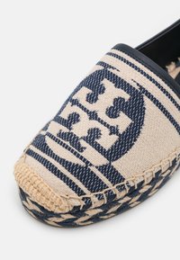 Chaussure espadrille tissée beige et bleu marine avec une semelle en jute tressée et un motif géométrique audacieux sur le tissu supérieur.