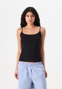 Black tank top with thin straps, made of smooth fabric. Worn with light blue striped shorts, displaying an elastic waistband.
