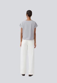 Haut gris à manches courtes et pantalon large blanc. Le haut présente des manches retroussées, et le pantalon a des poches arrière avec une texture lisse.