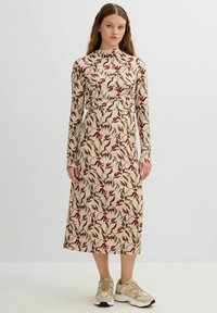 Vestido de manga larga con estampado floral en beige, con flores rojas y hojas verdes. Largo hasta la mitad de la pantorrilla, con corsé ajustado. Par de zapatillas beige.