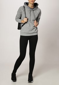 Szara bluza z kapturem i czarnymi sznurkami, w połączeniu z czarnymi legginsami i czarnymi trampkami. Prosty, casualowy design; brak widocznych wzorów.