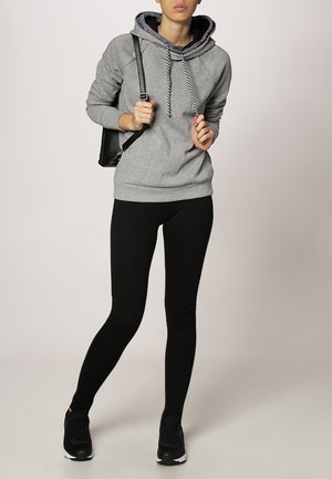 Sweatshirt à capuche gris avec des cordons noirs, associé à des leggings noirs et des baskets noires. Design simple et décontracté ; aucun motif visible.