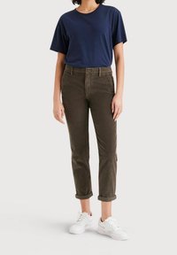 Marinblå t-shirt, bruna kordflöjtsbyxor med uppvikta avslut och vita sneakers. Fokus på avslappnade, texturerade material och enkel design.