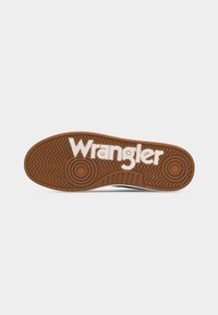Jalatsijalats pruunist kummist tallamustriga ja valge "Wrangler" logoga, mis on põhja peal selgelt reljeefne.