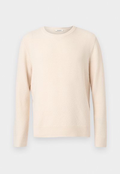 Μακρυμάνικη πλεκτή μπλούζα σε κρεμ χρώμα με υφασμένο σχέδιο, ριμπ μανσέτες και τελείωμα, και στρογγυλή λαιμόκοψη.