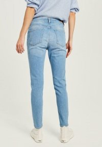 Smala jeans i ljusblå denim med hög midja, fem fickor och en jämn yta, tillsammans med vita högstövlar.