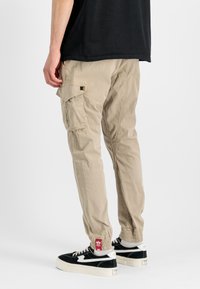 Kakhi cargo hlače z stranskimi žepi, elastičnimi manšetami in sproščenim krojem, v kombinaciji s črnimi in belimi supergami z semiš detajli.