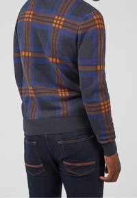 Pull en tricot gris présentant un motif à carreaux orange et bleu. Manches et ourlet côtelés, avec une coupe ajustée. Associé à un denim foncé.