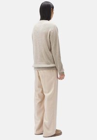 Beige Strickpullover mit strukturiertem Finish, kombiniert mit hellbeigen weiten Hosen. Das Outfit zeichnet sich durch schlichte Linien und eine lockere Passform aus.