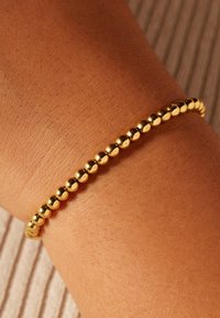 Gold beaded bracelet on skin, featuring smooth, spherical beads in a uniform pattern, with a polished finish and a flexible design.