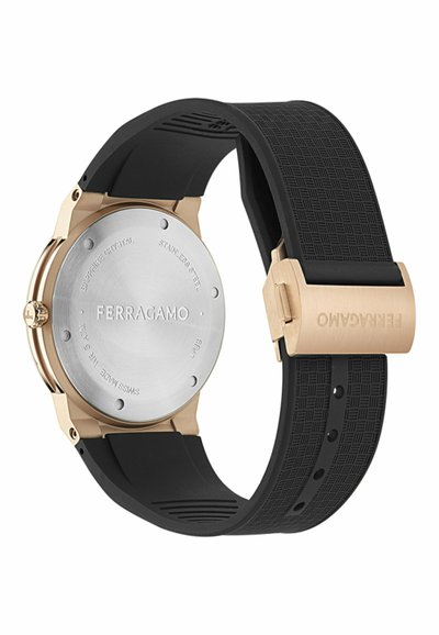 Zadná strana hodiniek Ferragamo s puzdrom z nehrdzavejúcej ocele, zlatistými detailmi, čiernym textúrovaným gumovým remienkom a značkovou prackou.