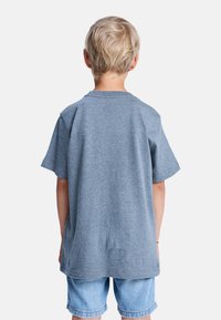 Szara bawełniana koszulka z krótkim rękawem, okrągłym dekoltem i luźnym krojem; noszona z jasnoniebieskimi dżinsowymi szortami. Widok z tyłu, bez grafik ani wzorów.