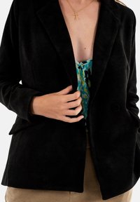 Blazer de pana negra con un diseño ligeramente estructurado, que cuenta con solapas de muesca y dos bolsillos frontales para un aspecto ajustado.