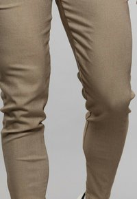 Pantalons beige ajustés en tissu texturé, présentant une finition lisse et des détails de couture minimaux pour une apparence épurée.