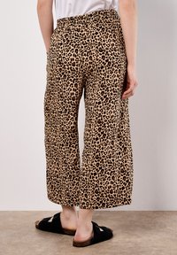 Pantalons larges à imprimé léopard avec une taille élastique, fabriqués en tissu doux. La texture est lisse, avec une palette de couleurs marron clair et noir.