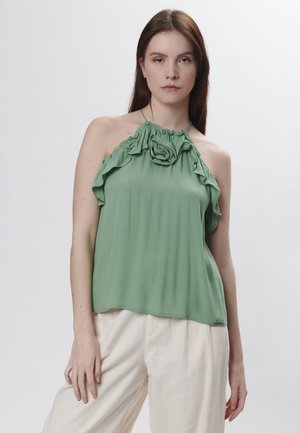 Groene mouwloze top met ruches en een bloemenaccent bij de halslijn, gemaakt van lichtgewicht stof, gecombineerd met lichtgekleurde broeken.